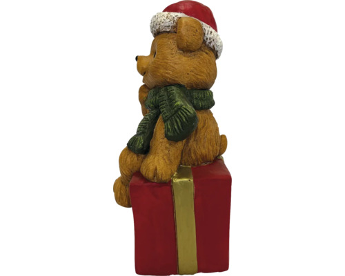 Weihnachtsfigur brauner Bär mit roter Nikolausmütze und grünem Schal sitzend auf einem roten Geschenkpaket.