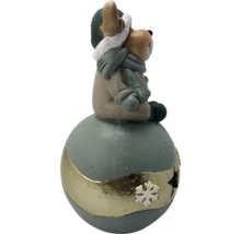 Figurine de Noël petit ours avec bonnet et écharpe assis sur une boule décorative avec décoration de flocon de neige.