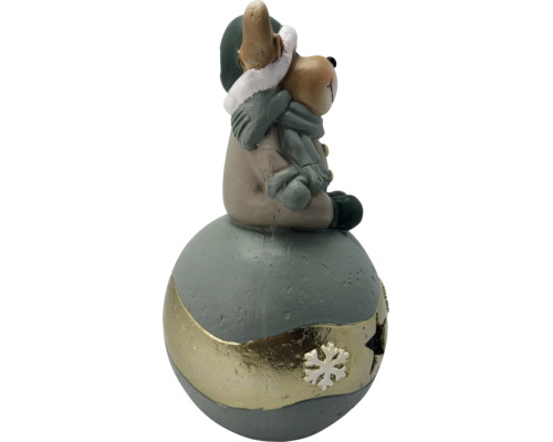 Figurine de Noël petit ours avec bonnet et écharpe assis sur une boule décorative avec décoration de flocon de neige.