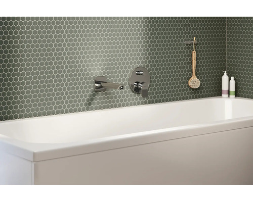 Salle de bain moderne avec mosaïque hexagonale verte au mur derrière une baignoire blanche avec robinetterie chromée.