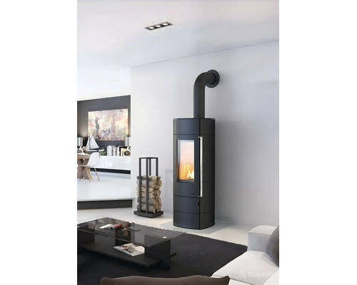 Moderner schwarzer Kaminofen mit grossem Sichtfenster und brennendem Feuer in einem hellen Wohnzimmer neben einem Kaminholzregal.