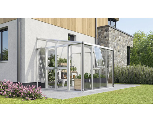 Serre adossée moderne en aluminium et verre, fixée au mur d'une maison sur une terrasse avec des plantes à l'intérieur.