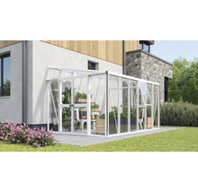 Serre adossée en aluminium et verre contre un mur de maison, avec porte coulissante et lucarne sur une terrasse avec des plantes de jardin.