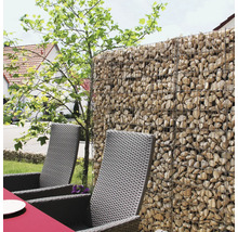 Mur de gabions rempli de pierres naturelles servant de brise-vue dans un jardin avec des chaises en rotin synthétique.