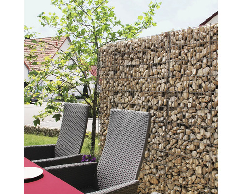 Mur de gabions rempli de pierres naturelles servant de brise-vue dans un jardin avec des chaises en rotin synthétique.
