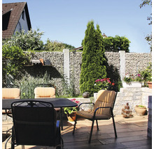 Salon de jardin sur une terrasse avec mur en gabions, chaises avec coussins et table sur sol avec aspect bois.