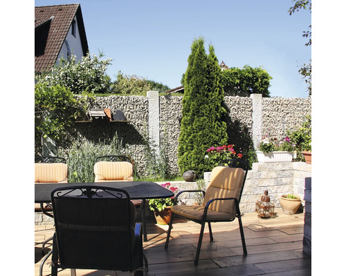 Salon de jardin sur une terrasse avec mur en gabions, chaises avec coussins et table sur sol avec aspect bois.
