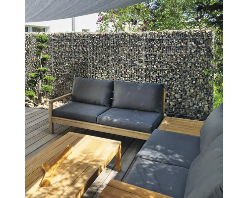 Salon de jardin moderne sur terrasse en bois avec mur de gabions, meubles en bois avec coussins gris et table basse assortie.