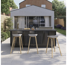 Moderne Außenküche auf gepflasterter Terrasse mit integrierter Spüle, Grill und drei Barhockern mit Holzbeinen vor einem hellen Gebäude.