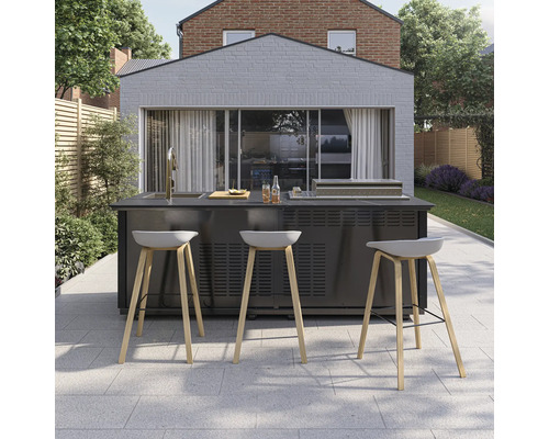 Moderne Außenküche auf gepflasterter Terrasse mit integrierter Spüle, Grill und drei Barhockern mit Holzbeinen vor einem hellen Gebäude.