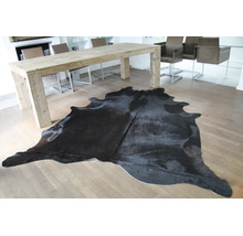Ein schwarzes Kuhfell auf hellem Parkett in einem hellen, modernen Esszimmer mit grossem Holztisch.