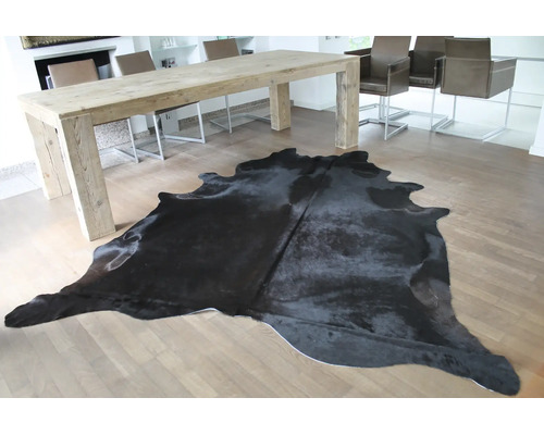 Ein schwarzes Kuhfell auf hellem Parkett in einem hellen, modernen Esszimmer mit grossem Holztisch.