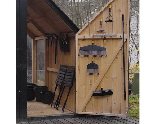 Hell und organisiert eingerichtetes Gartenhaus aus Holz mit Gartengeräten an der Tür sowie Klappstühlen und Pflanztöpfen im Inneren.