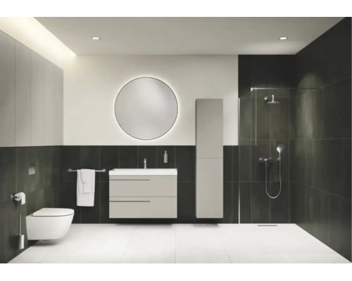 Modernes Badezimmer mit Waschtischunterschrank, Hochschrank, rundem beleuchtetem Spiegel, Wand-Toilette und begehbarer Dusche mit dunklen Fliesen.