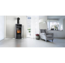 Helles, modernes Wohnzimmer mit einem schwarzen Kaminofen mit sichtbarem Feuer, einem grauen Sessel und einer Glastür nach draußen.