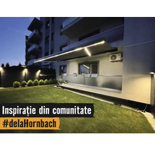 Store banne éclairé avec bandes LED intégrées au-dessus d'un balcon avec garde-corps en verre et pelouse entretenue la nuit.