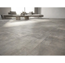 Modernes Wohnzimmer mit großformatigen Bodenfliesen in Betonoptik, grauem Sofa und Holztisch.