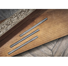 Drei Metallverbinder für Laminat- oder Parkettbodenleisten auf einer Holzoberfläche.