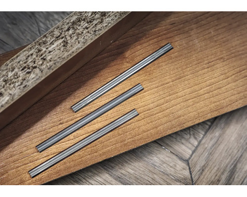 Drei Metallverbinder für Laminat- oder Parkettbodenleisten auf einer Holzoberfläche.