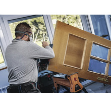 Handwerker schleift eine Holztür mit einem Akku-Exzenterschleifer in einer hellen Werkstatt.