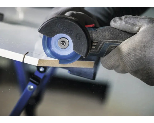 Un outil multifonction sans fil Bosch utilisé pour découper une plaque de bois avec un disque à tronçonner par une main gantée.