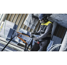 Artisan équipé de protections coupe un tube métallique avec une meuleuse d angle sans fil sur un établi pliant.