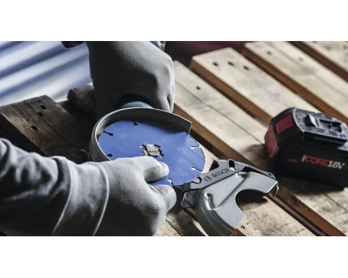 Personne avec des gants changeant le disque de tronçonnage d une meuleuse d angle sans fil Bosch sur une palette en bois
