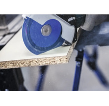 Scie circulaire manuelle coupant un panneau de particules revêtu sur une table de travail.