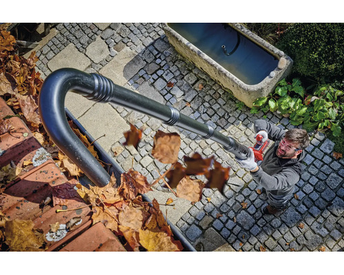 Un homme nettoie une gouttière depuis le sol avec un accessoire de souffleur de feuilles à batterie.