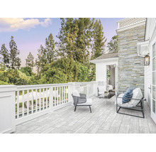 Terrasse spacieuse avec des carreaux en pierre naturelle, une balustrade en bois blanc et des meubles de salon modernes devant une façade en pierre.