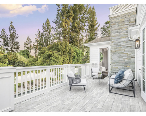 Terrasse spacieuse avec des carreaux en pierre naturelle, une balustrade en bois blanc et des meubles de salon modernes devant une façade en pierre.