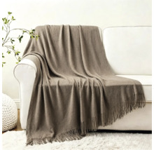 Eine weiche Wohndecke mit Fransen liegt über einer weißen Couch in einem modern eingerichteten Wohnzimmer.