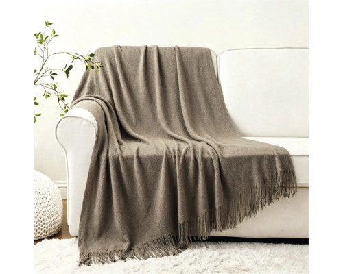 Eine weiche Wohndecke mit Fransen liegt über einer weißen Couch in einem modern eingerichteten Wohnzimmer.