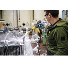 Ein Mitarbeiter reinigt eine industrielle Anlage in einem Betrieb mit einem Hochdruckreiniger und Schaumsprühkopf von Kärcher.