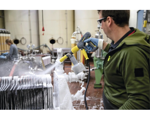 Ein Mitarbeiter reinigt eine industrielle Anlage in einem Betrieb mit einem Hochdruckreiniger und Schaumsprühkopf von Kärcher.
