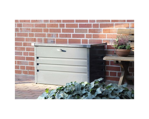 Graue Gartentruhe aus Metall vor einer Ziegelwand.