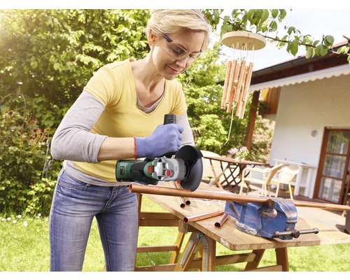 Frau arbeitet im Garten mit einem Winkelschleifer an einem Kupferrohr, das in einem Schraubstock befestigt ist