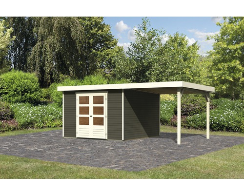 Abri de jardin Karibu Kodiak 6 avec extension de toit 558 x 331 cm gris terre Abri de jardin avec annexe sur une surface pavée dans un jardin.