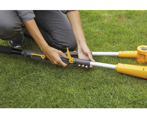 Une personne assemble un outil de jardin jaune à l''extérieur.