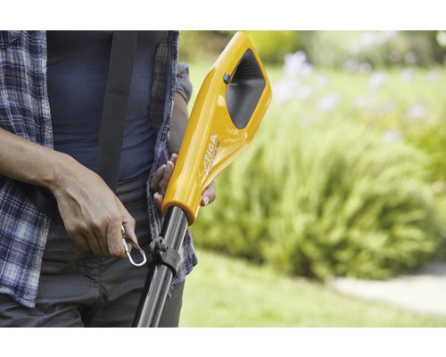 Gros plan d''une personne tenant un coupe-bordure jaune avec une bandoulière, avec un espace vert en arrière-plan