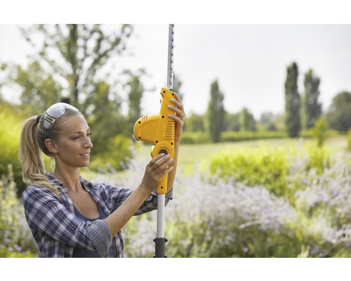 Une femme utilise un taille-haie télescopique à batterie dans le jardin