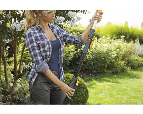 Une femme portant des lunettes de sécurité manipule un ébrancheur dans le jardin.
