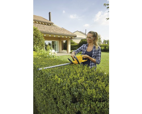 Frau schneidet Hecke mit einer Heckenschere im Garten.