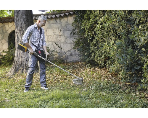Ein Mann benutzt einen Akku-Rasentrimmer im Garten, um Gras zu schneiden.