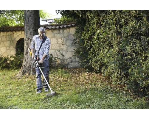 Mann schneidet Gras mit einem Rasentrimmer im Garten.