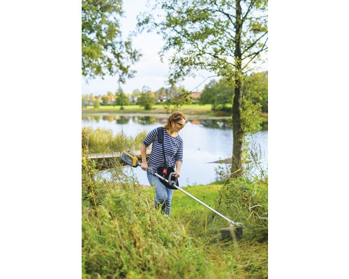 Frau benutzt Rasentrimmer im Garten am See.