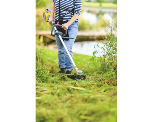Eine Person benutzt einen Rasentrimmer im Garten, um das Gras zu schneiden.