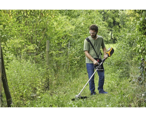 Ein Mann verwendet einen Rasentrimmer zur Gartenpflege in einem begrünten Bereich.