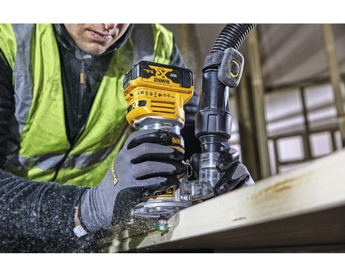 Un homme fraise une planche de bois avec une défonceuse sans fil. Un tuyau d''aspiration est raccordé. Marque : DeWalt