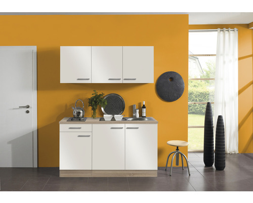 Cuisine avec évier, plaque de cuisson et armoires murales devant un mur ocre